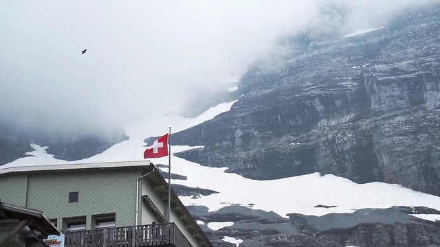 Swiss Flag waving dramatically with birds flying in slow motion at Eigergletscher mountains