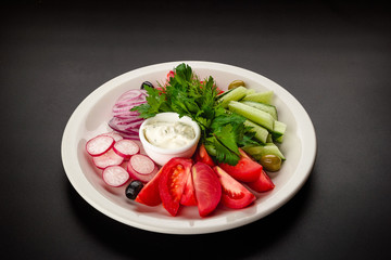 Sliced vegetables lie on a black plate on a black background photographed. Vegetables are photographed horizontally.