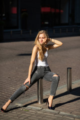 Obraz na płótnie Canvas Attractive blonde woman with long hair wearing jeans and t shirt posing at the city in sun rays