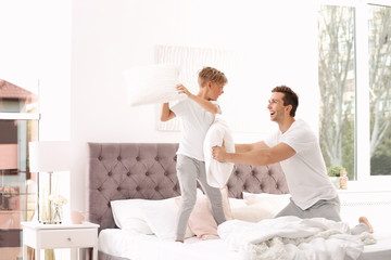 Father and son having pillow fight on bed at home