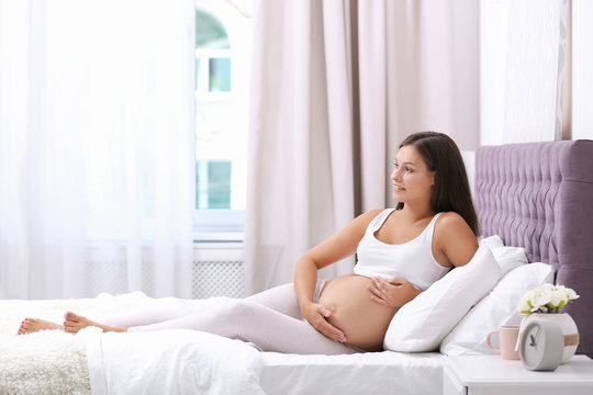 Happy pregnant woman lying on bed at home