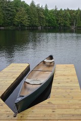 Sagamore Lake, Adirondack Park, New York, USA: A canoe tied to a wooden dock on a lake surrounded by evergreen trees.