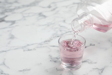 Pouring mouthwash in glass and space for text on marble background. Teeth care