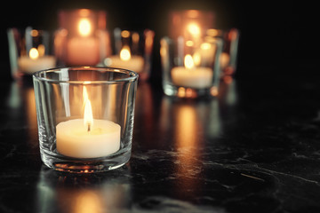 Burning candle on table in darkness, space for text. Funeral symbol