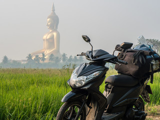 Large sitting Buddha above the palm trees and rice fields with scooter on foreground. The biggest Buddha of Thailand. Ang Thong province, Thailand. Bike Travel Concept © Oleksandr