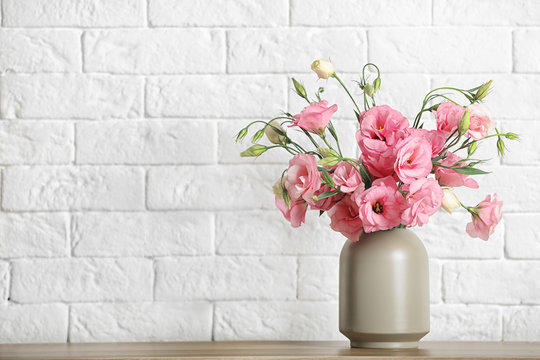 Vase with beautiful flowers on table against brick wall, space for text