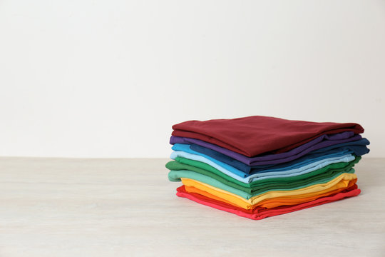 Stack of bright folded clothes on table against white background. Space for text