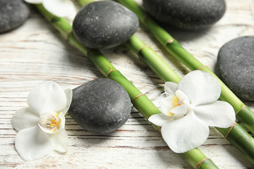 Fototapeta na wymiar Bamboo branches, spa stones and flowers on wooden background