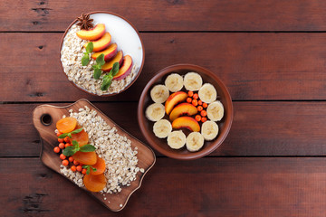 Oatmeal with fruits and green mint. Oat flakes with milk and dried apricots on wooden background. Healthy food for vegans. Dry oats with peaches, anise and berries of mountain ash