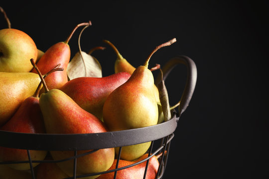 Basket with ripe pears on black background, closeup. Space for text