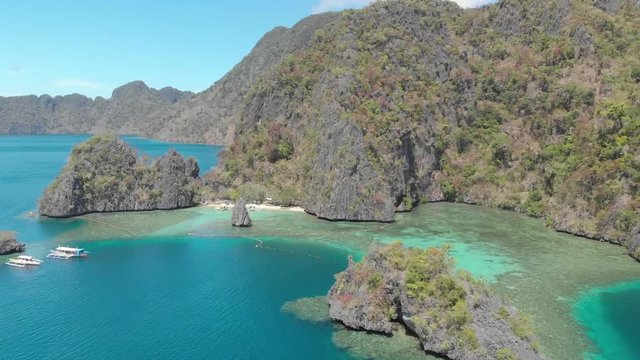 Aerial drone shot over turquoise lagoons, and towards limestone cliffs and paraw boats, on a paradise isle, on a sunny day, at Coron island, Philippines, Asia