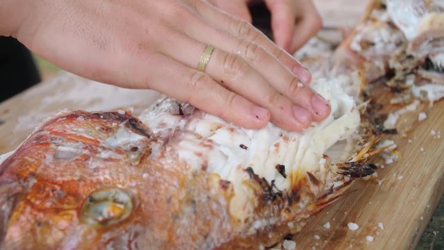 Close up on hands, hands removing meat from grilled red sea bream