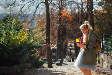 A beautiful girl is standing with an autumn leaf in her hands in a park in Paris