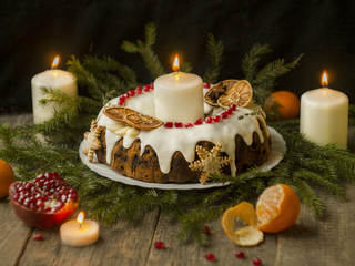 Christmas English fruitcake with candied fruit, dried fruit and nuts, decorated with white icing on a wooden background with fir branches, candles. Festive English cuisine