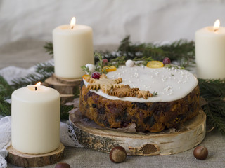 Christmas English fruitcake with candied fruit, dried fruit and nuts, decorated with white icing on a wooden background with fir branches, candles. Festive English cuisine
