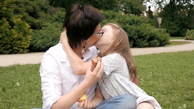 Happy Mother and Daughter gently hug and kiss sitting on a Blanket at Park Picnic