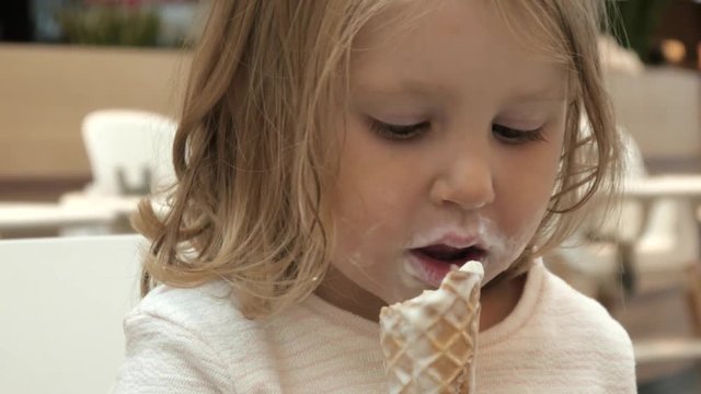 Little Girl Child eats an Ice Cream Cone sitting in a Mall Cafe
