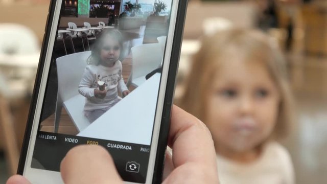 Mother makes Photo by iPhone of a little Child Daughter eats an Ice Cream