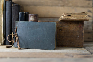 Old books and a wooden box set on a shelf. Old publishing houses set side by side on a wooden table.
