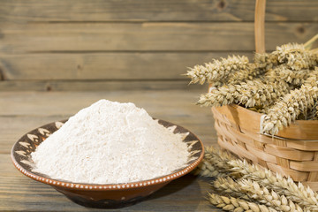 Harvest of wheat spikelets and flour on wooden background