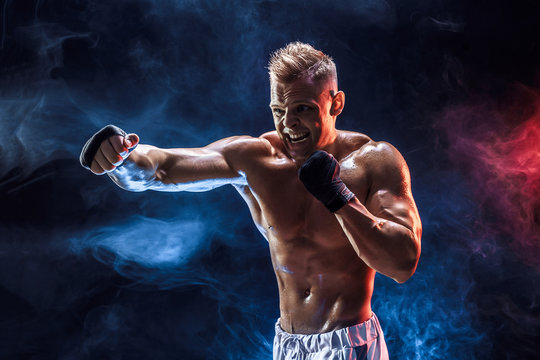 Studio portrait of fighting muscular man in smoke on dark background
