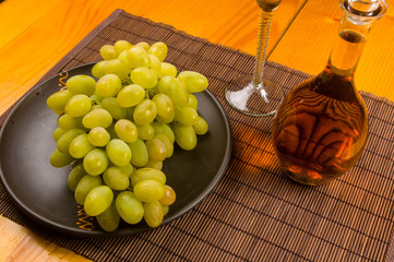 large brush of green grapes in a ceramic plate, a decanter and a glass of wine and cheese
