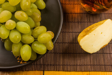 large brush of green grapes in a ceramic plate, a decanter and a glass of wine and cheese