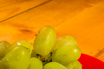 large brush of green grapes in a red ceramic plate on a wooden background