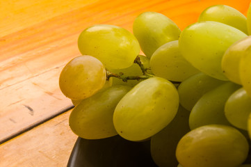 large brush of green grapes in a dark ceramic plate on a wooden background