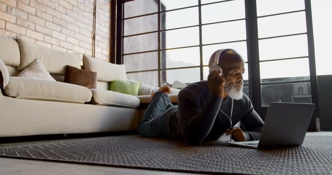 Senior man listening music on laptop in living room 4k