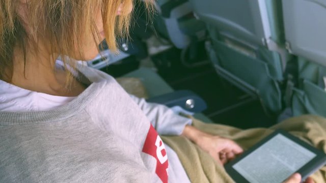Woman reading ebook sitting inside airplane, travel vacation technology concept