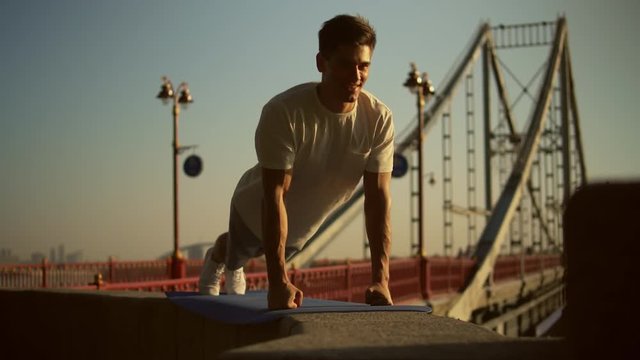 guy wearing white t-shirt is having street workout. sportsman does push ups on the fists.