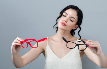 Young woman comparing two eye glasses on a gray background