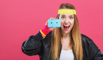 Woman in 1980's fashion holding a cassette tape on a pink background