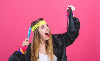 Woman in 1980's fashion playing a cowbell on a pink background