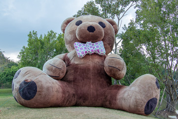 Naklejka premium The giant plush teddy bear sitting on a green meadow in the garden.