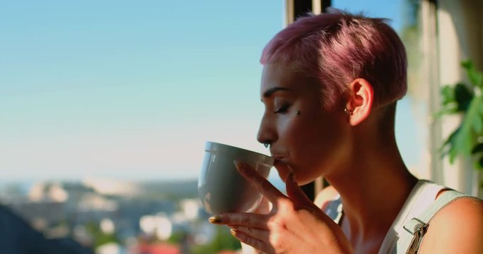 Woman having cup of coffee and looking through window 4k