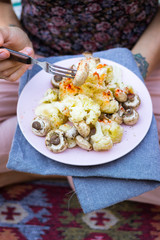 Steamed, cooked vegetables. Woman holds in hands on legs. Above view. Cauliflower, mushrooms with paprika. Vegan lunch, vegetarian dinner, healthy food