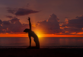Silhouette of woman practice yoga on the beach at sunset
