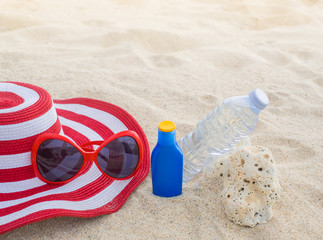 Sunscreen, hat, sunglasses and bottle of water on sand beach