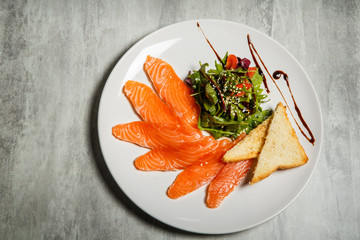 top view on salmon slices served with rucola and tomato salad and toasted bread