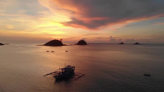 Aerial drone shot over a paraw boat, towards a red sunset sky, above the ocean, in Philippine archipelago, on a sunny warm evening dusk, at Nacpan beach, on Palawan island, in Philippines, Asia