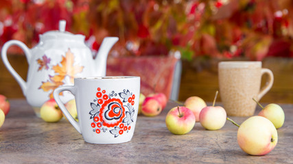 Cup of tea with autumn leaves and apples on wooden table