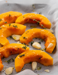 Sliced pumpkin with greens and sea salt on white baking paper as background. Top view. Copy space.