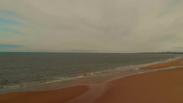 Beautiful views from drone of a long wide beach during low tide under a blue cloudy sky with some views of a family walking along.