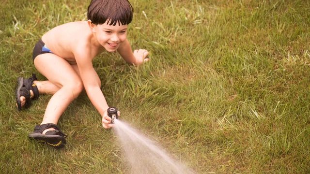 Cinemagraph looking down on a boy in a swimsuit spraying water with a background of grass.