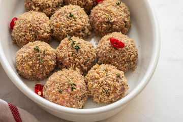 Raw fresh meatballs in the white plate on the white table. Copy space.