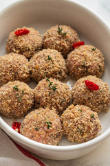 Raw fresh meatballs in the white plate on the white table. Copy space.