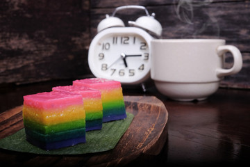 Traditional Malaysian food. Kuih Lapis , alarm clock and  a cup of coffee on wooden background....