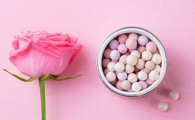 Cosmetic pearl make up powder with brush and fresh rose on pink pastel background. Top view.